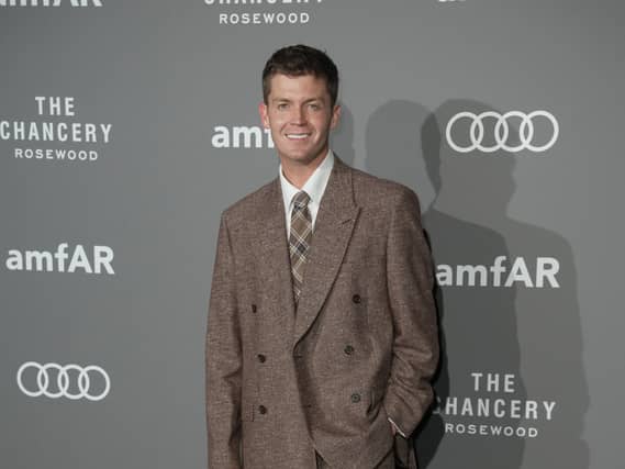 Jamie Miller smiling while posing for photos at a red carpet event, wearing a brown suit